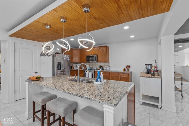 kitchen featuring appliances with stainless steel finishes, tasteful backsplash, light stone counters, sink, and pendant lighting