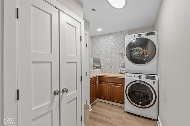 laundry area featuring cabinets, light wood-type flooring, stacked washer / dryer, and sink