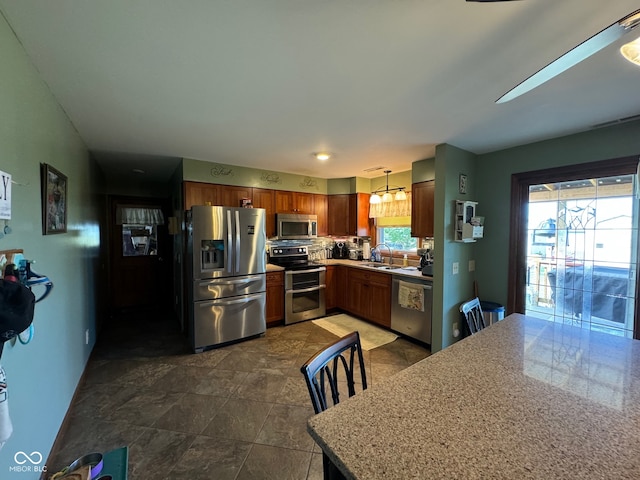 kitchen featuring light stone counters, sink, decorative light fixtures, and appliances with stainless steel finishes