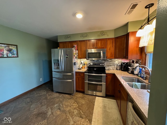 kitchen featuring light stone counters, sink, backsplash, pendant lighting, and appliances with stainless steel finishes