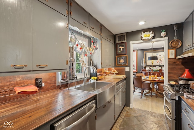 kitchen with appliances with stainless steel finishes, sink, tasteful backsplash, and wood counters