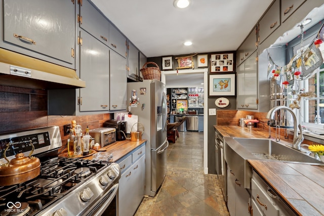 kitchen with wooden counters, decorative backsplash, gray cabinets, sink, and stainless steel appliances