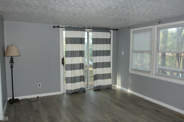 unfurnished room with a wealth of natural light, dark wood-type flooring, and a textured ceiling