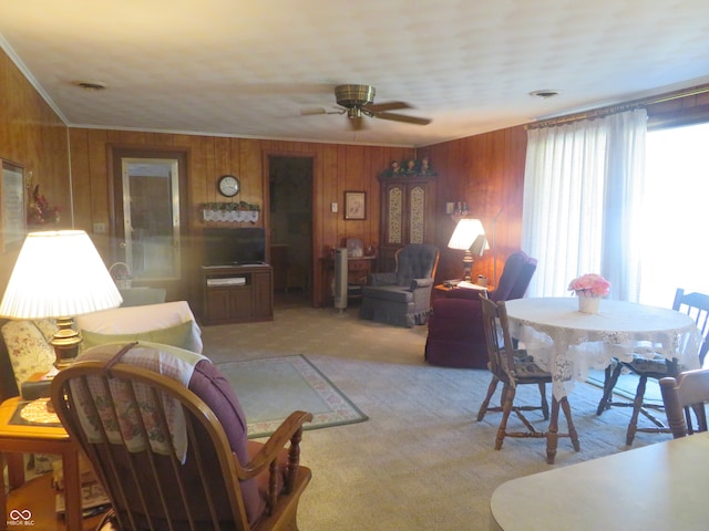 living room featuring ornamental molding, wood walls, ceiling fan, and carpet flooring