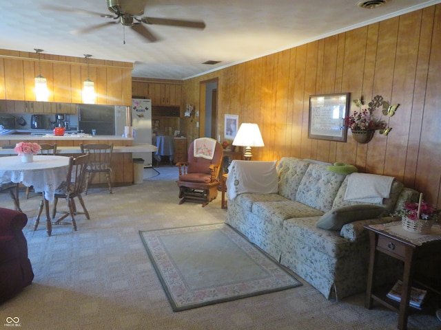 carpeted living room with ceiling fan, ornamental molding, and wooden walls