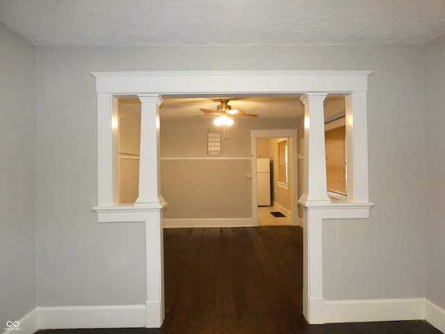 empty room featuring a textured ceiling, wood-type flooring, ornate columns, and ceiling fan