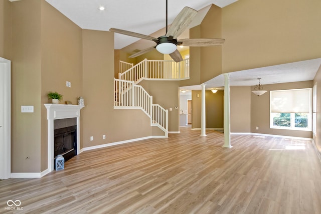 unfurnished living room featuring light hardwood / wood-style floors, a tiled fireplace, high vaulted ceiling, and ornate columns