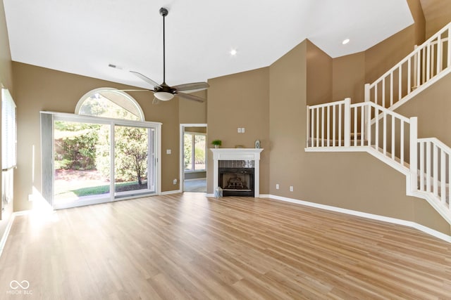 unfurnished living room with a towering ceiling, light wood-type flooring, and ceiling fan