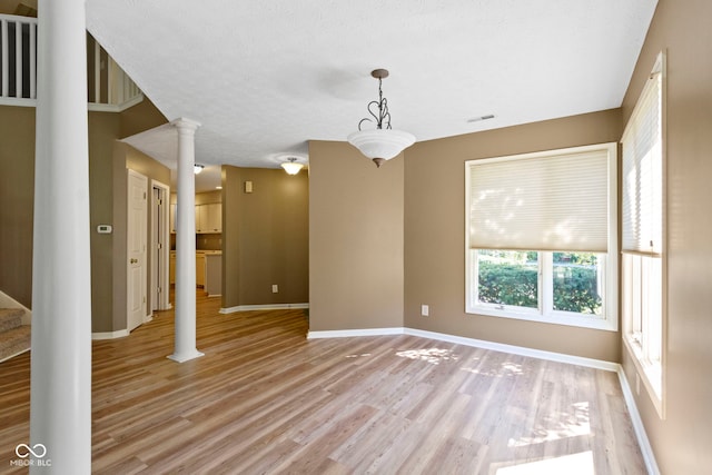 empty room with light hardwood / wood-style flooring, a textured ceiling, and ornate columns