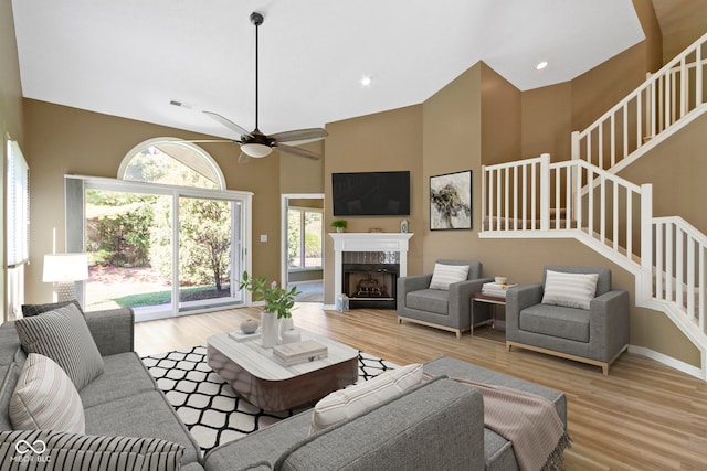 living room featuring ceiling fan, a towering ceiling, and light wood-type flooring