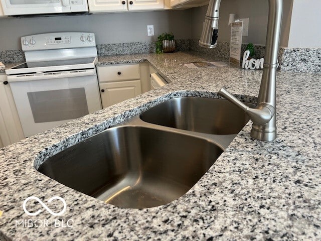 kitchen with sink, white cabinets, light stone counters, and white appliances