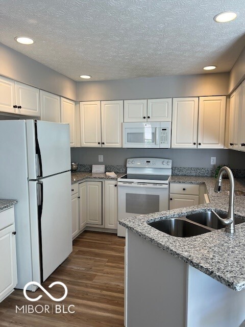 kitchen with white cabinetry, light stone countertops, dark wood-type flooring, and white appliances