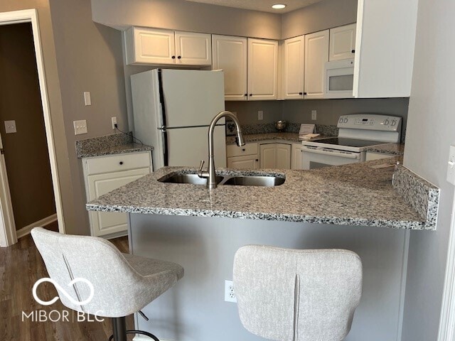 kitchen with a breakfast bar area, kitchen peninsula, sink, light stone counters, and white appliances