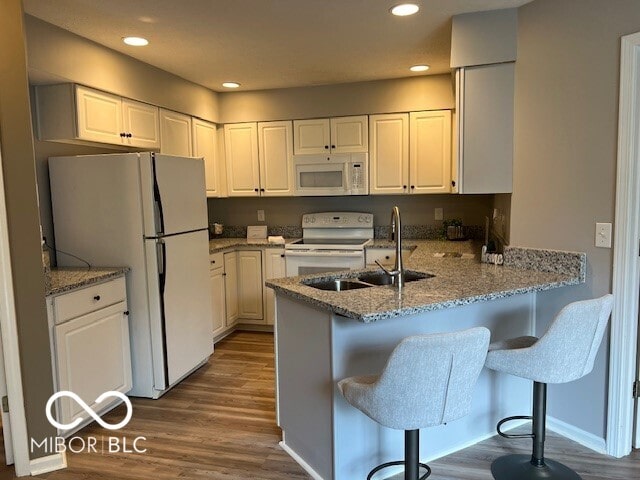 kitchen with dark wood-type flooring, white cabinets, kitchen peninsula, and white appliances