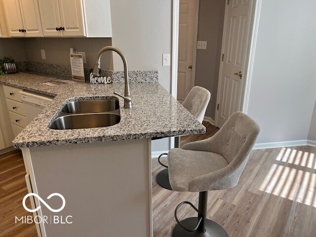 kitchen with sink, light wood-type flooring, kitchen peninsula, light stone counters, and a breakfast bar area