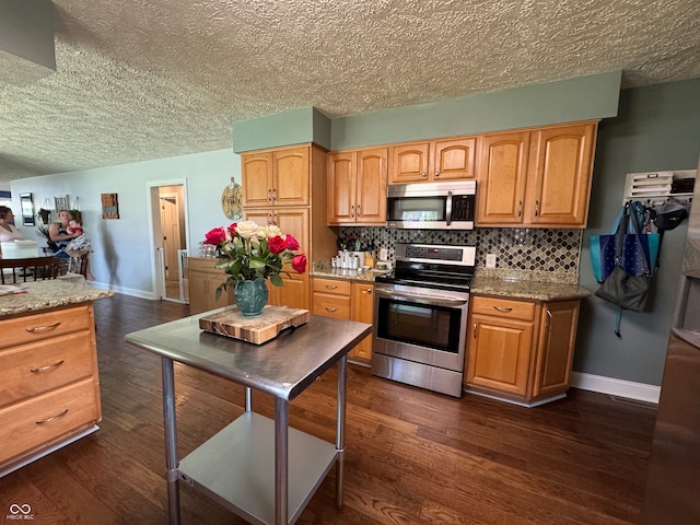 kitchen featuring dark wood-type flooring, light stone countertops, appliances with stainless steel finishes, and decorative backsplash