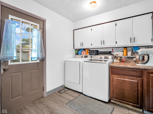 clothes washing area featuring baseboards, washer and dryer, light wood-style floors, cabinet space, and a textured ceiling