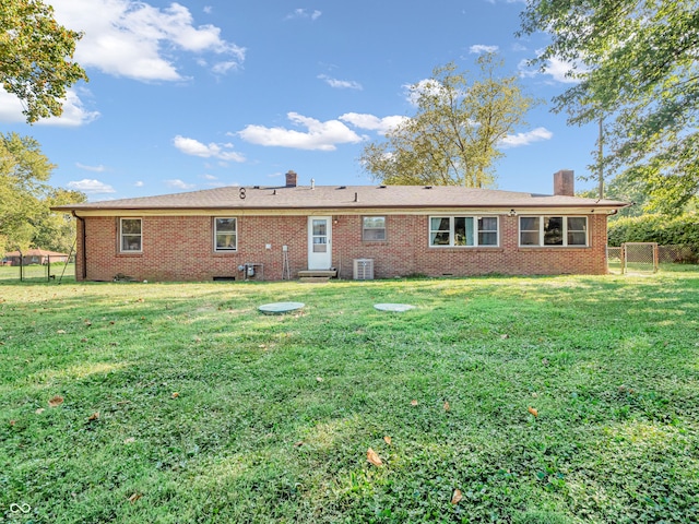 rear view of property with a lawn, brick siding, central AC, and a chimney