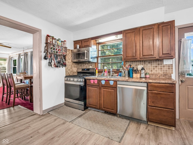 kitchen with light wood-style flooring, appliances with stainless steel finishes, brown cabinets, and a sink