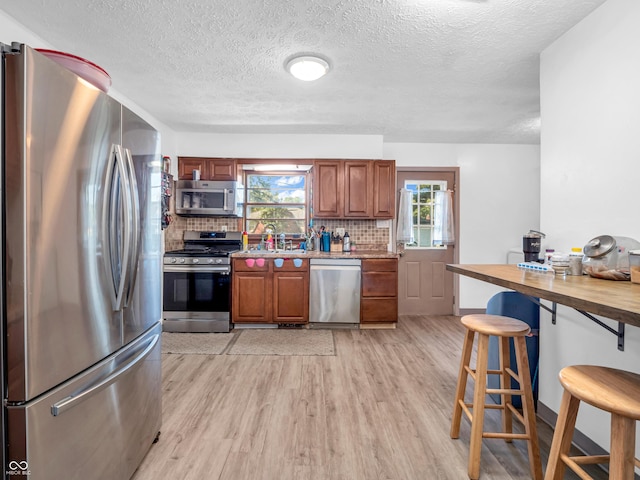 kitchen with light wood finished floors, tasteful backsplash, wooden counters, a breakfast bar area, and appliances with stainless steel finishes