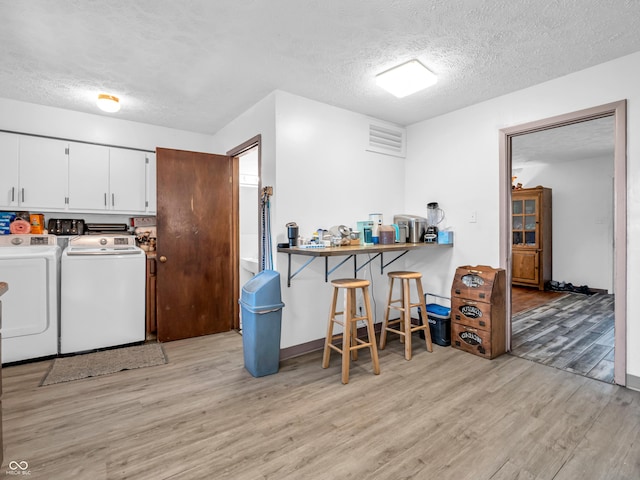 laundry area featuring cabinet space, a textured ceiling, light wood-style flooring, and washer and clothes dryer