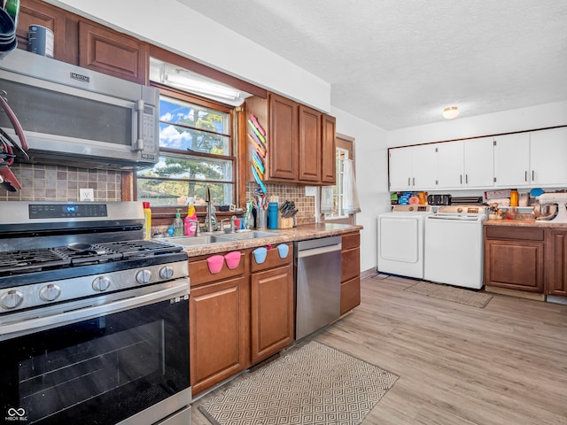 kitchen with light wood finished floors, washing machine and clothes dryer, a sink, stainless steel appliances, and light countertops