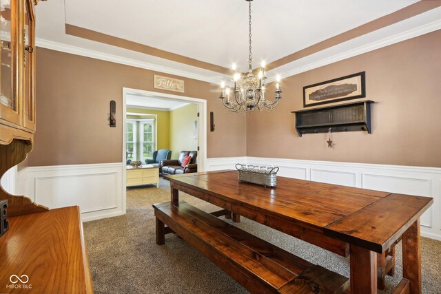 carpeted dining area featuring ornamental molding, a tray ceiling, and an inviting chandelier