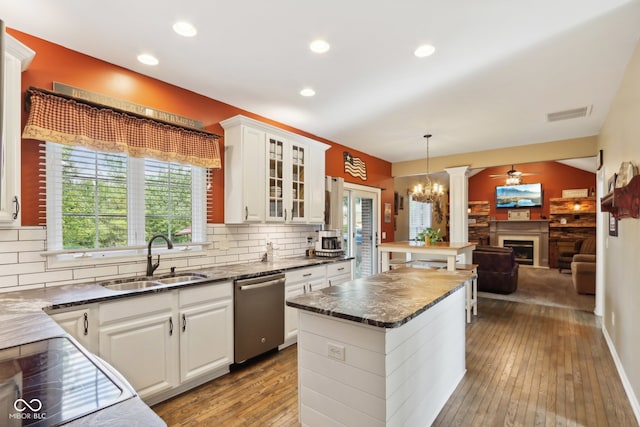 kitchen with light wood-type flooring, a kitchen island, sink, hanging light fixtures, and stainless steel dishwasher