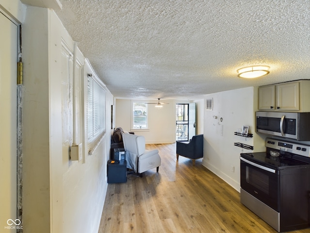 kitchen with a textured ceiling, hardwood / wood-style floors, stainless steel appliances, and ceiling fan