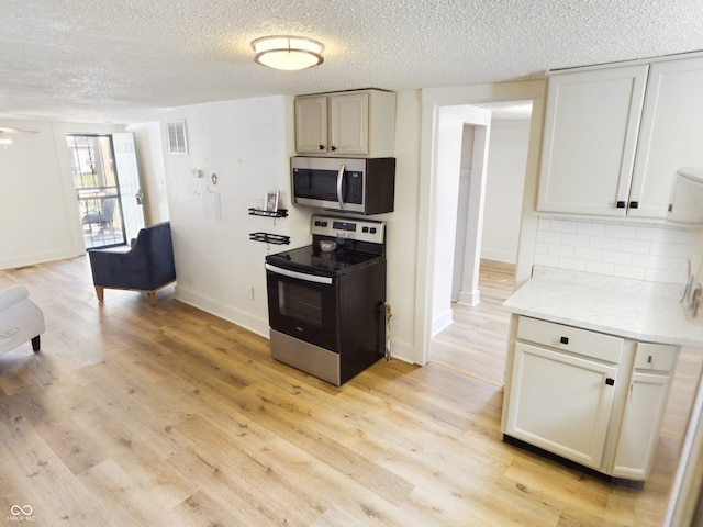 kitchen with light wood-type flooring, stainless steel appliances, decorative backsplash, and a textured ceiling