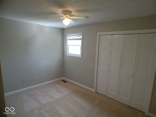 unfurnished bedroom featuring a textured ceiling, a closet, ceiling fan, and light carpet