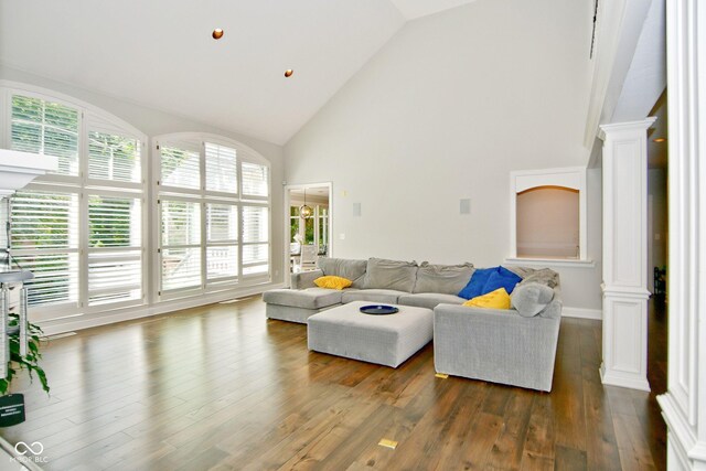 living room featuring dark wood-type flooring, high vaulted ceiling, and ornate columns