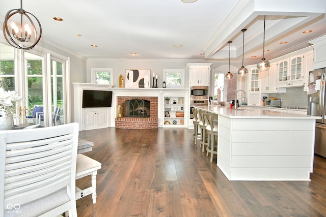 kitchen with an island with sink, white cabinetry, ornamental molding, and dark hardwood / wood-style flooring