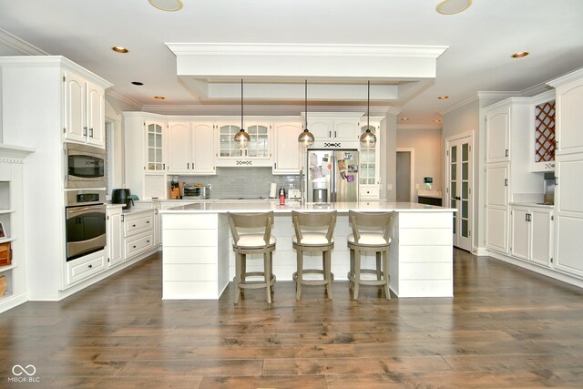 kitchen featuring dark hardwood / wood-style floors, a center island with sink, appliances with stainless steel finishes, crown molding, and white cabinetry