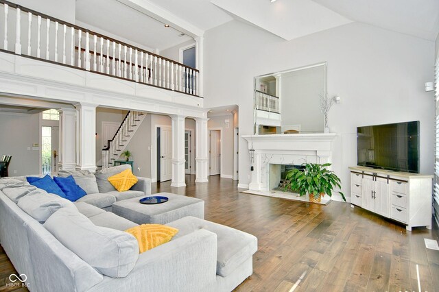 living room with high vaulted ceiling, dark hardwood / wood-style floors, a high end fireplace, and ornate columns