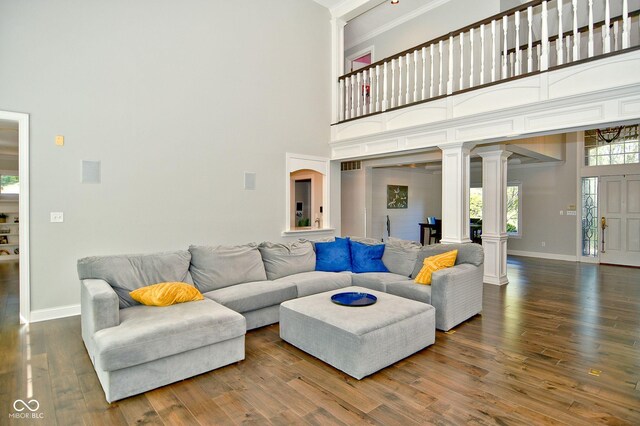 living room featuring dark wood-type flooring, decorative columns, ornamental molding, and a high ceiling