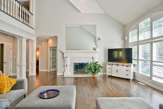 living room featuring a fireplace, crown molding, ornate columns, dark hardwood / wood-style floors, and high vaulted ceiling