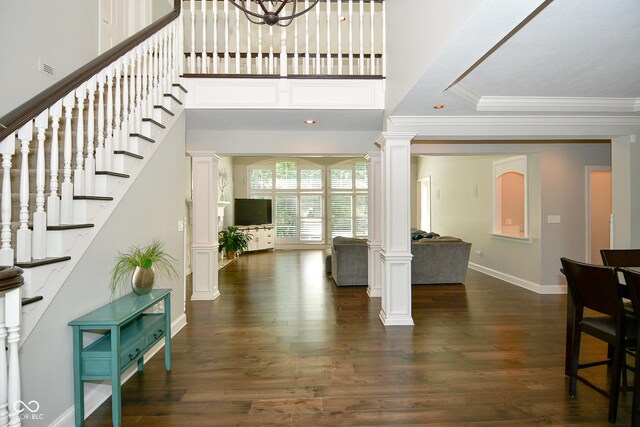 foyer entrance with dark hardwood / wood-style floors, ornamental molding, and ornate columns