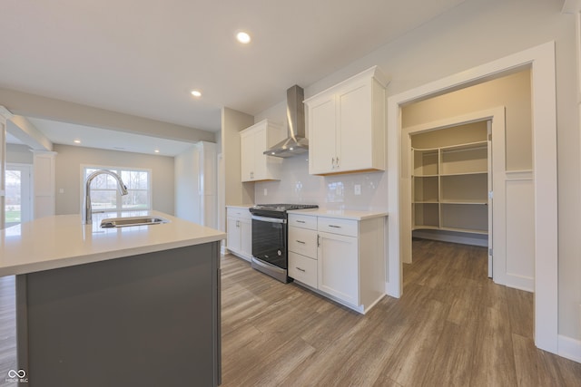 kitchen with wall chimney exhaust hood, stainless steel range, sink, a center island with sink, and white cabinetry