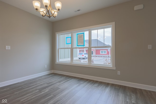 empty room with hardwood / wood-style floors and a notable chandelier