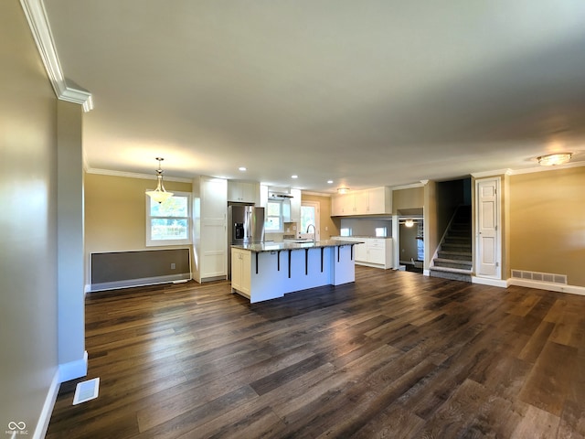 kitchen featuring dark wood-type flooring, pendant lighting, a center island with sink, white cabinetry, and a breakfast bar area