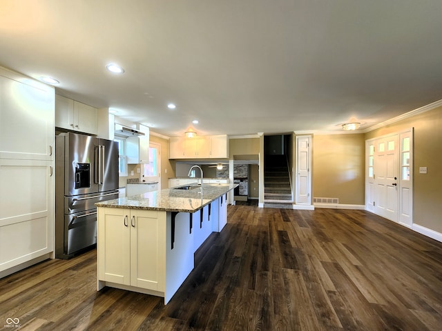 kitchen with dark wood-type flooring, light stone counters, high quality fridge, a center island with sink, and white cabinets