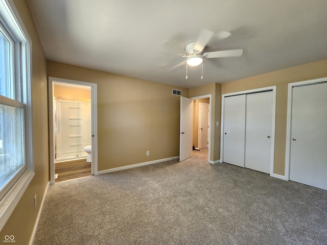 unfurnished bedroom with carpet flooring, two closets, ensuite bath, and ceiling fan