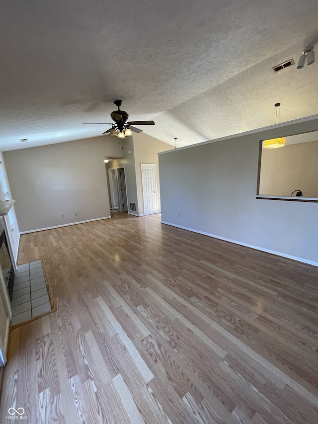 unfurnished living room featuring light wood-type flooring, vaulted ceiling, ceiling fan, and a textured ceiling