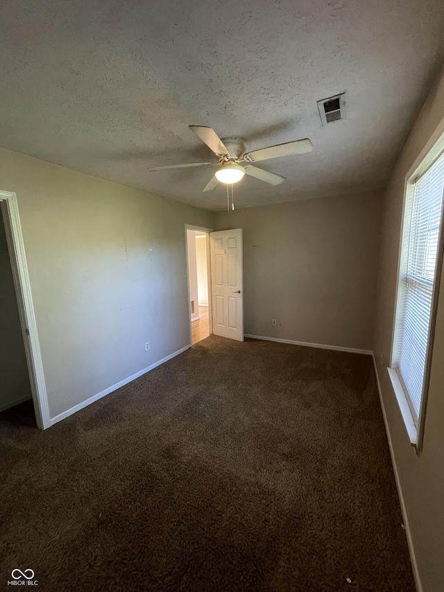 empty room featuring a textured ceiling, dark colored carpet, and ceiling fan