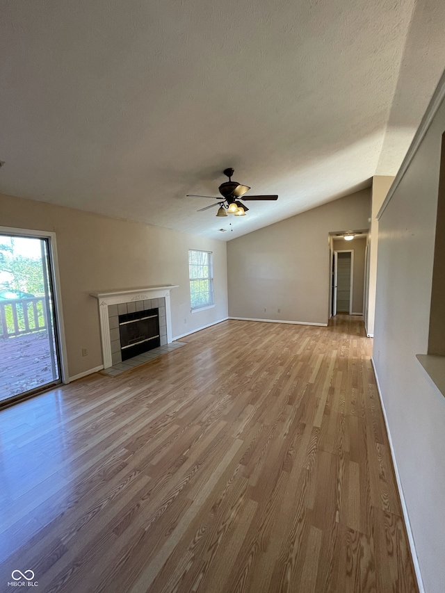 unfurnished living room with light hardwood / wood-style floors, ceiling fan, a textured ceiling, a tile fireplace, and vaulted ceiling