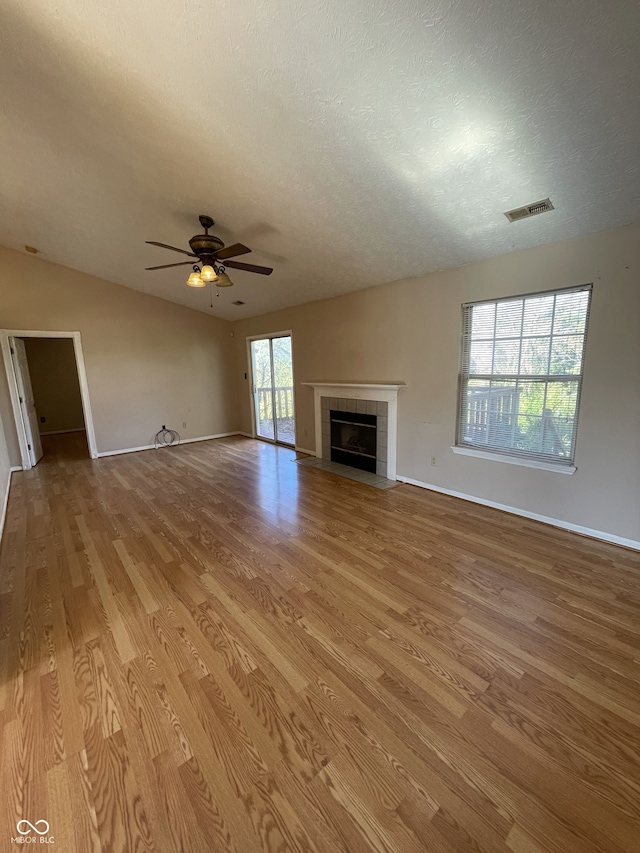 unfurnished living room featuring a wealth of natural light, a tiled fireplace, and light hardwood / wood-style floors