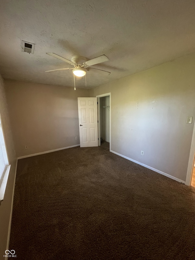 unfurnished room with a textured ceiling, ceiling fan, and dark carpet