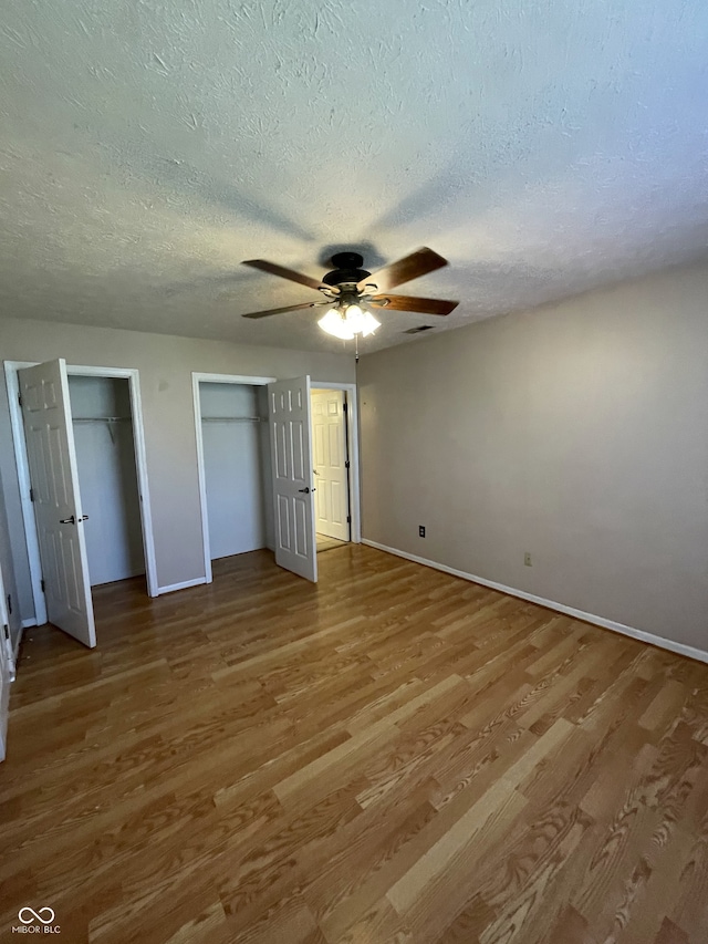 unfurnished bedroom featuring two closets, hardwood / wood-style flooring, ceiling fan, and a textured ceiling