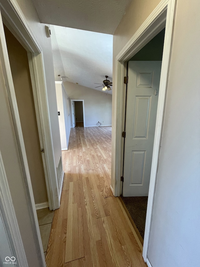 corridor with light wood-type flooring and vaulted ceiling